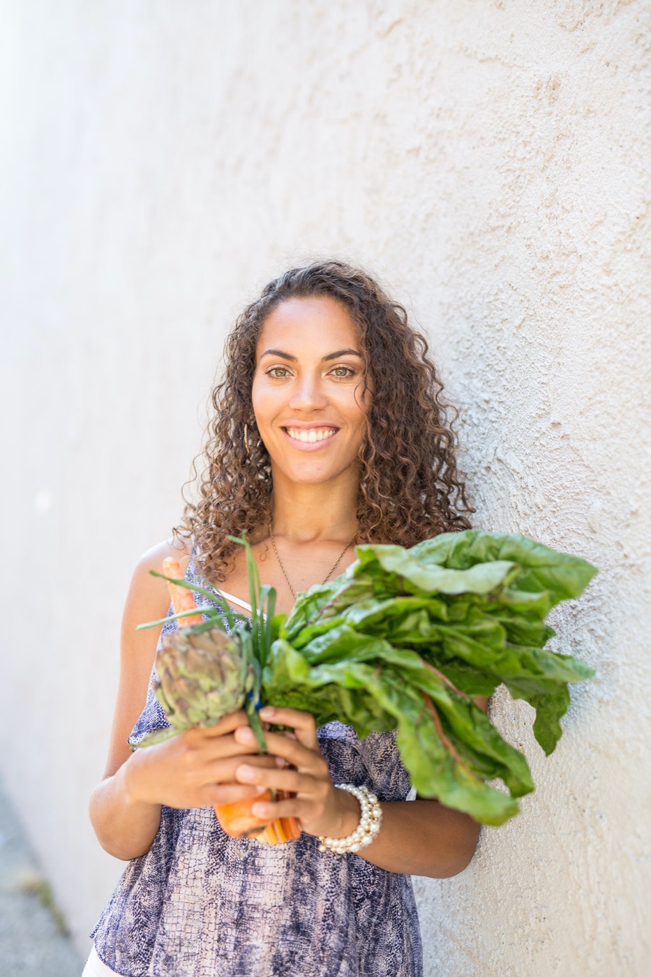 Donica smiling with an armful of fresh leafy greens and vegetables