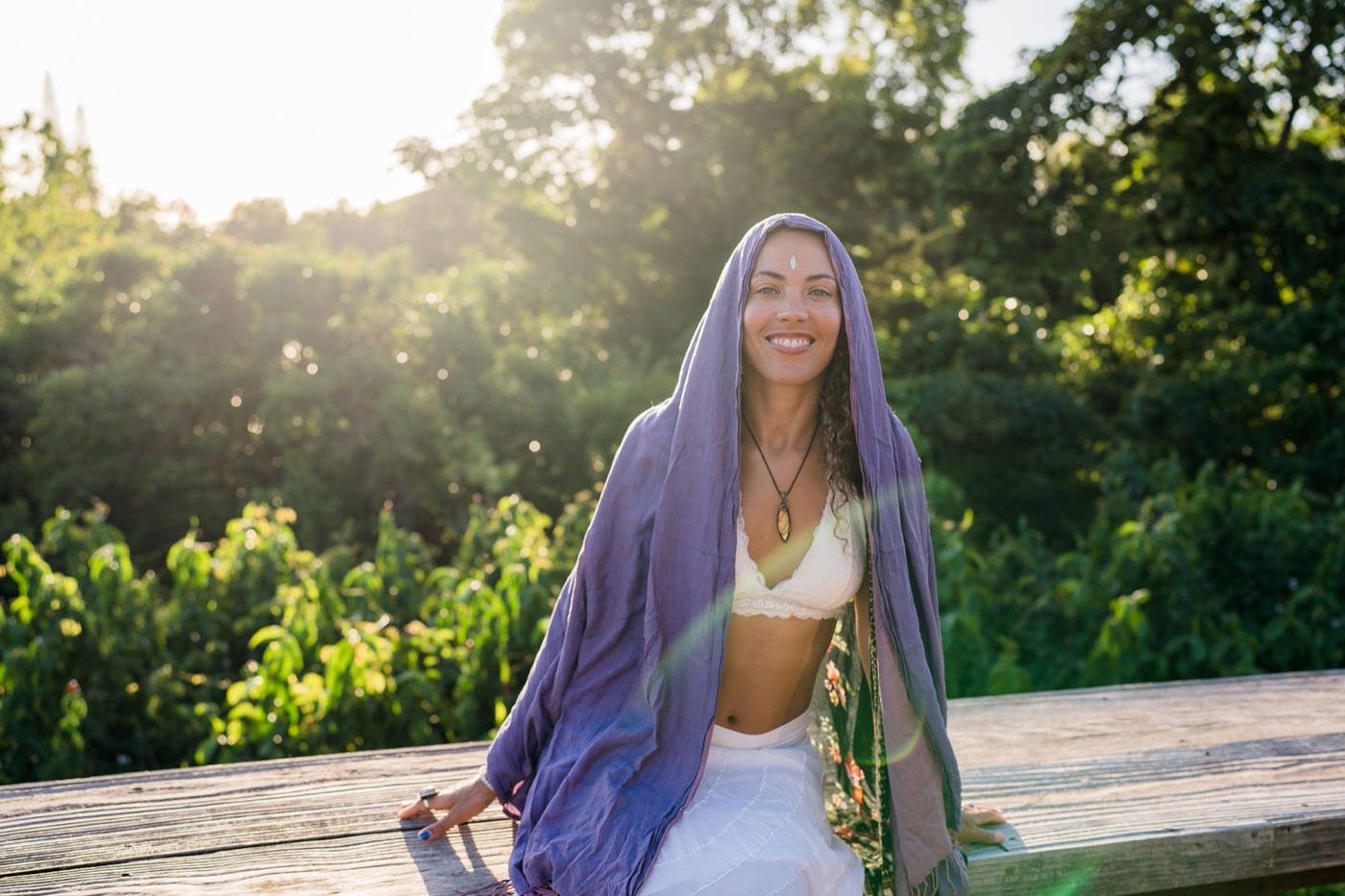 Donica smiling softly in a lavender veil, bathed in golden light with greenery behind her